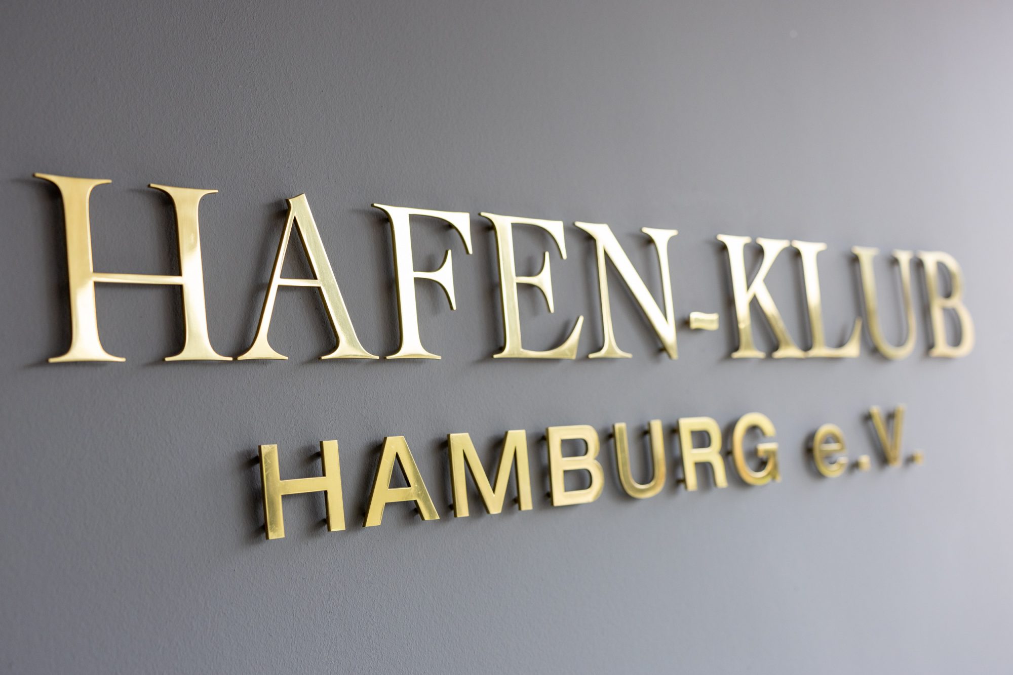 Gold-coloured Hafen-Klub Hamburg e. V. lettering on a grey wall.