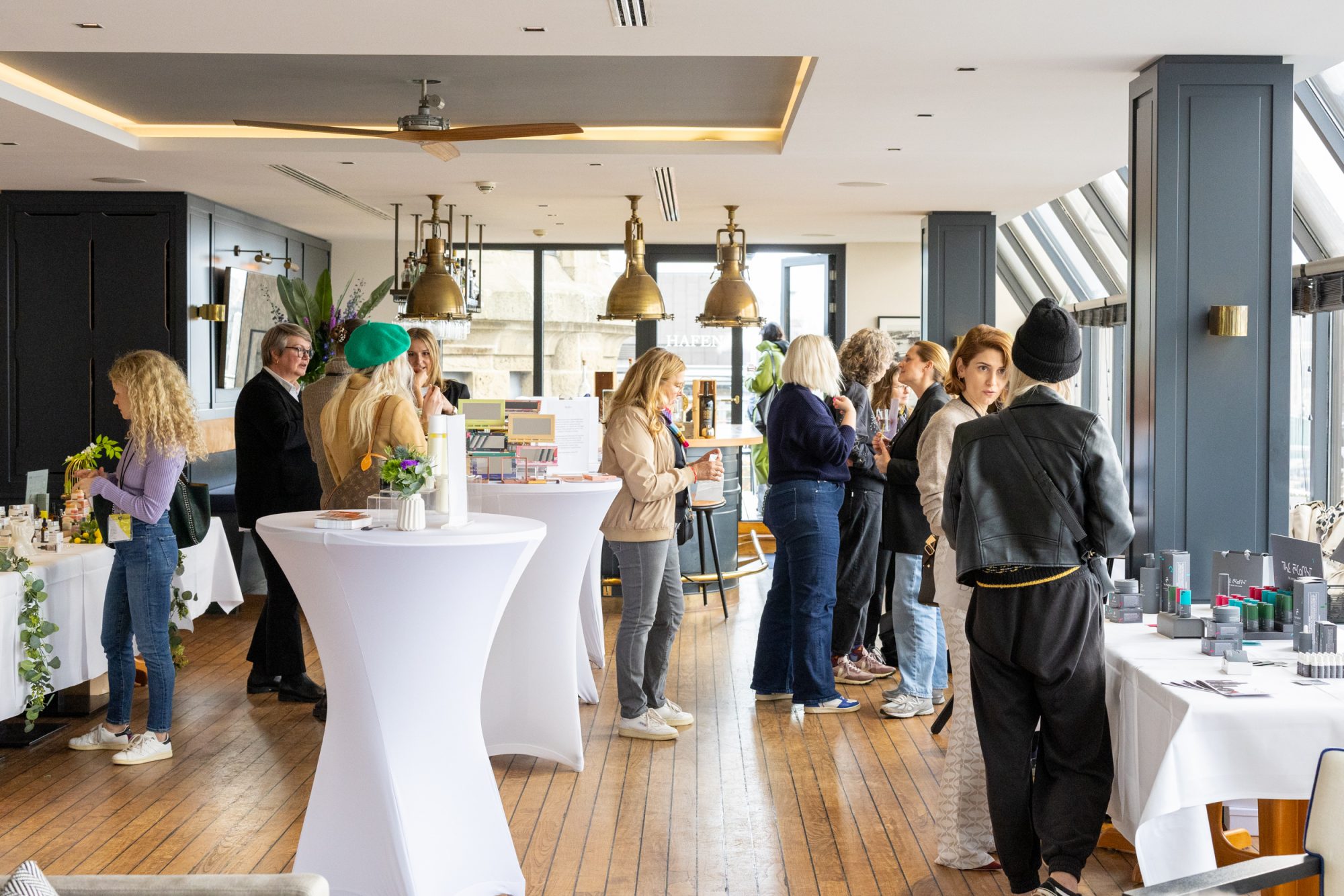 Guests talking among product displays and white standing tables at the beauty brunch in Hafen-Klub.
