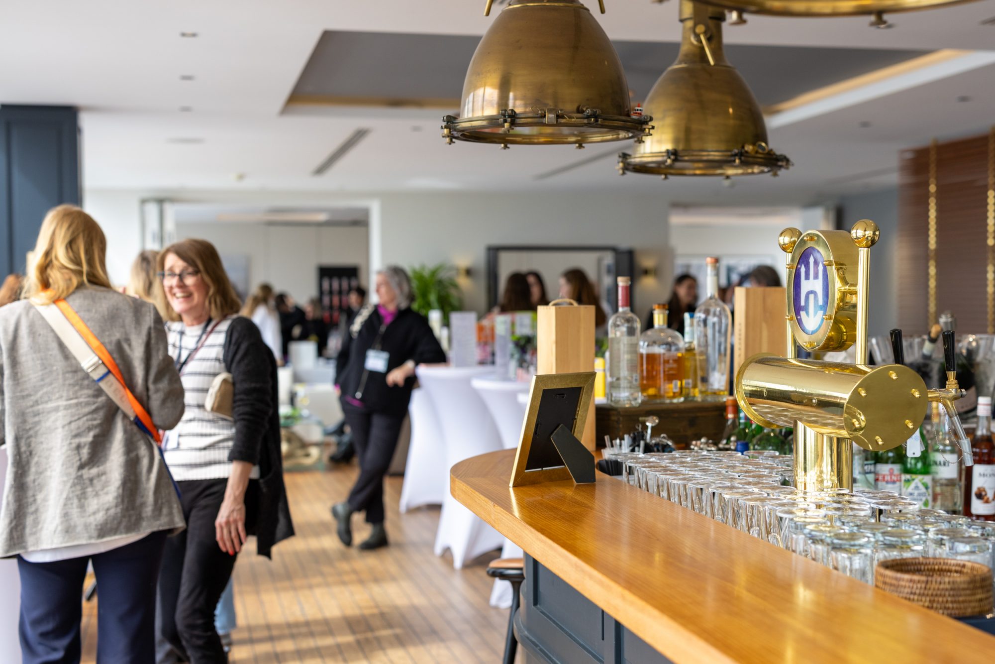 Guests talking beside the bar with brass pendant lights at the beauty brunch.