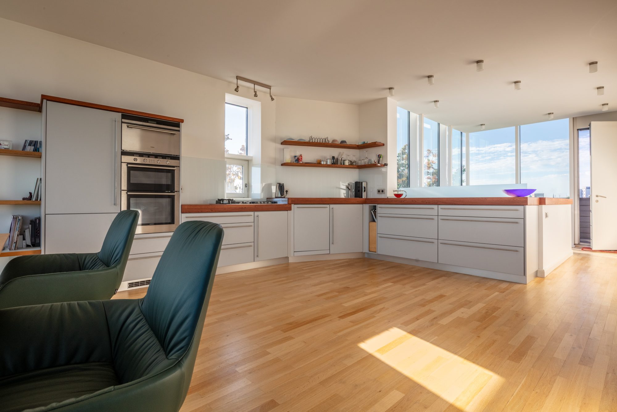 Offene Küche mit hellen Schrankfronten, Holzarbeitsflächen und angrenzendem Essbereich im lichtdurchfluteten Penthouse.