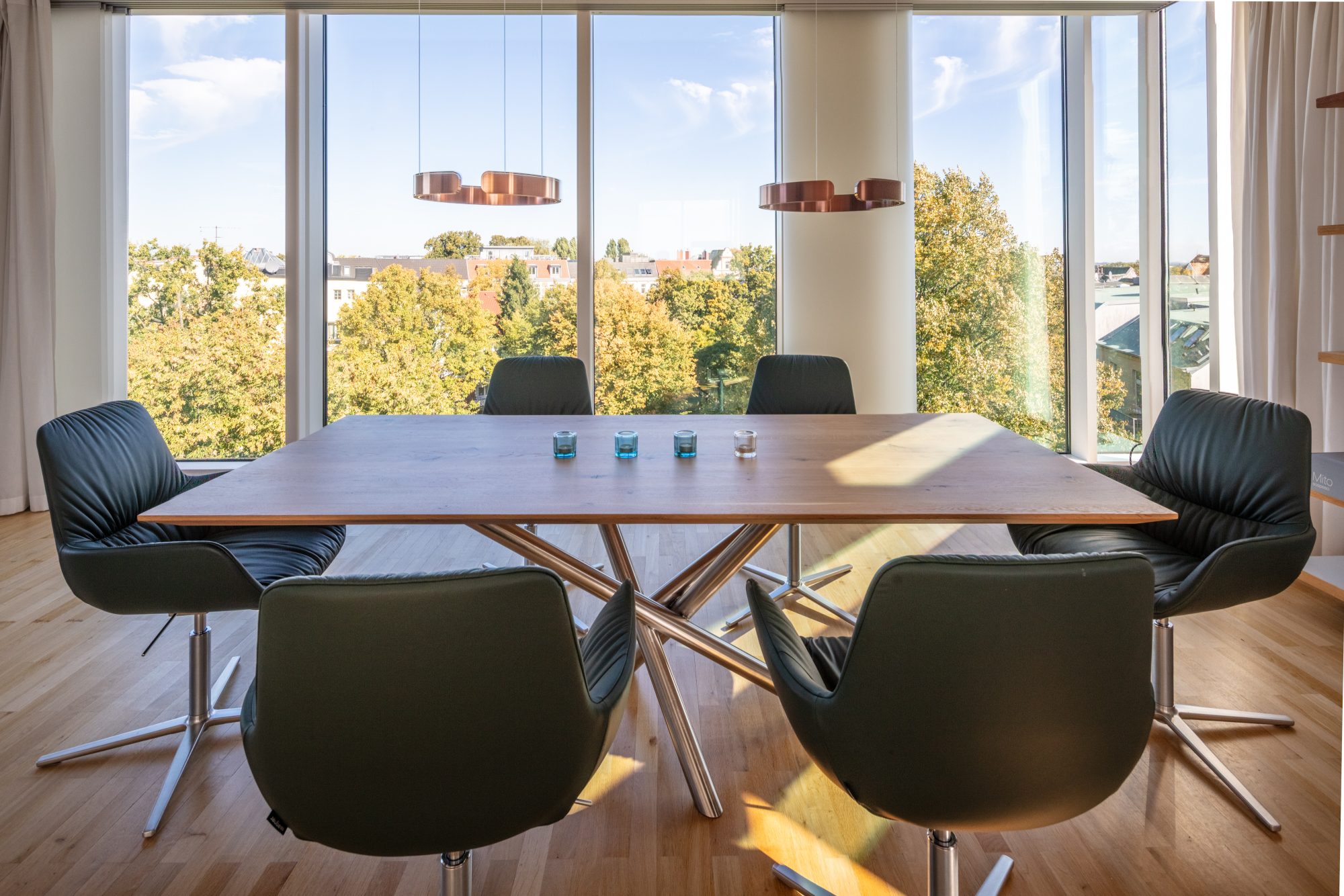 Esstisch mit sechs dunklen Stühlen und zwei Pendelleuchten vor einer raumhohen Fensterfront mit Blick auf Bäume und Dächer.