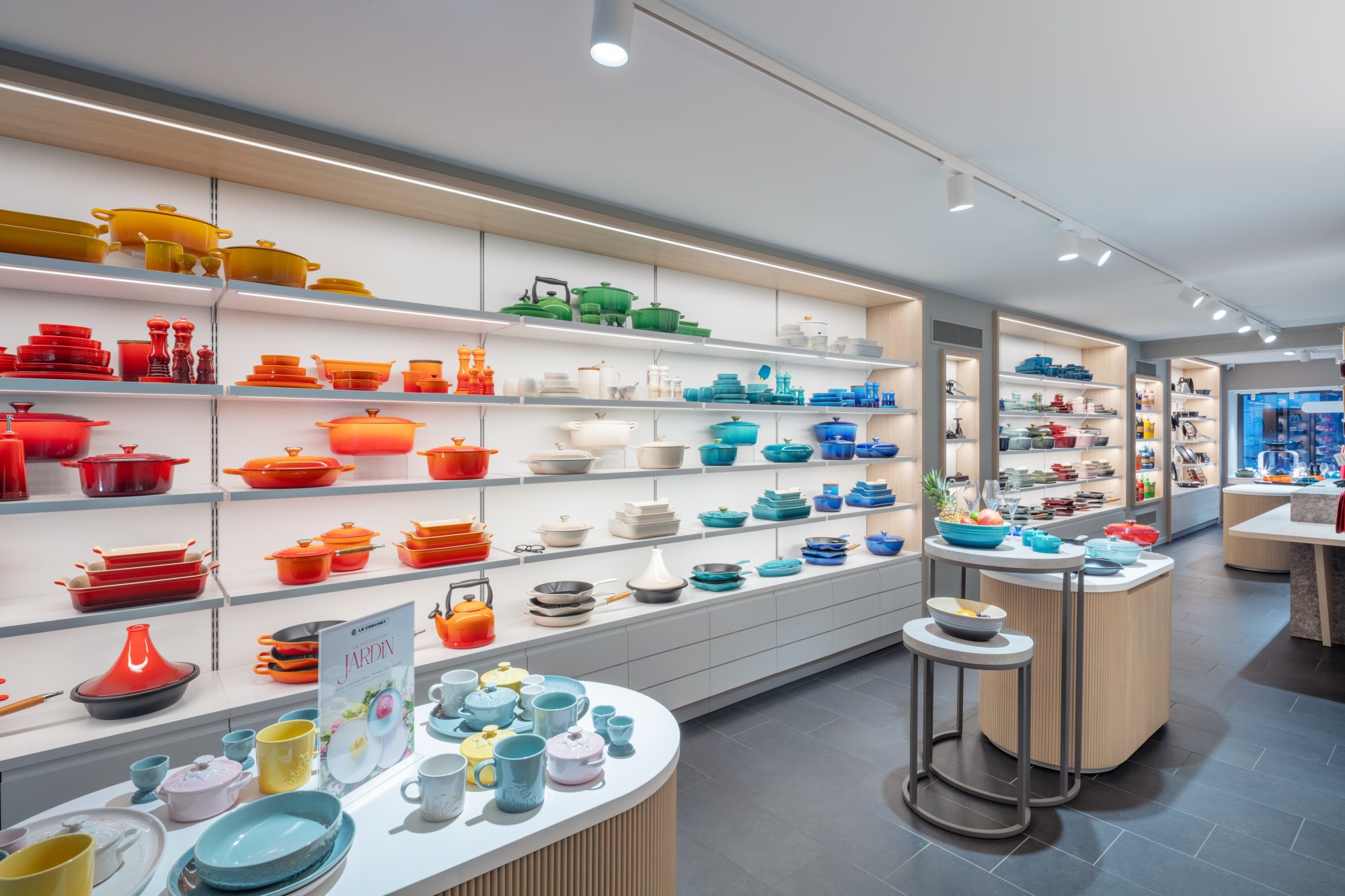 Beleuchtete Regalwand mit roten, orangefarbenen, weißen, türkisen und blauen Töpfen und Formen in der Le Creuset Boutique Basel.