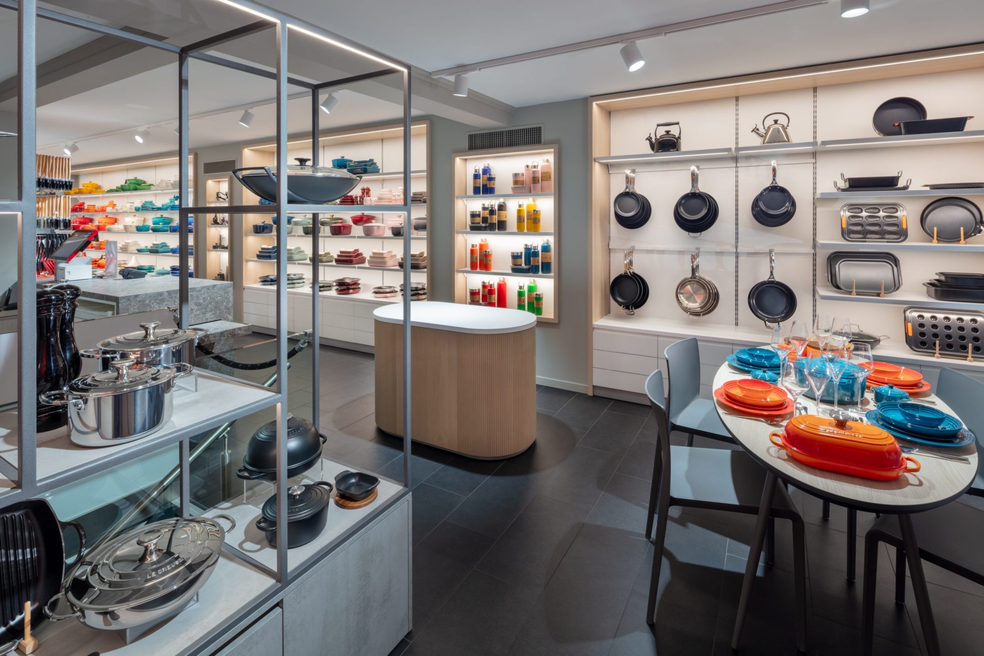 Display area in the Le Creuset boutique in Basel, with frying pans and bakeware on the wall, stainless steel cookware and a set dining table.