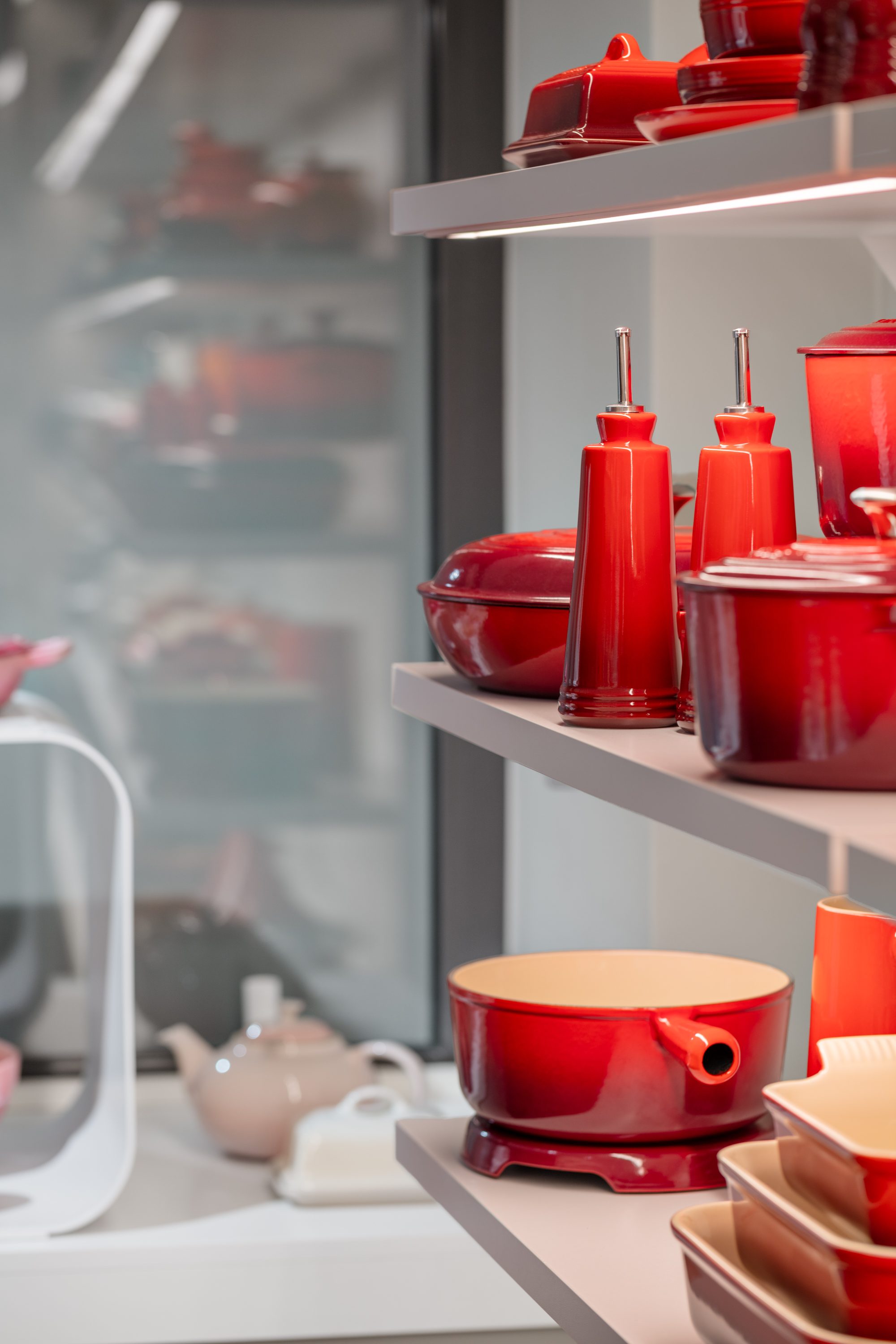Detail eines beleuchteten Regals mit roten Le Creuset Schalen, Vorratsgefäßen und Flaschen mit Ausgießern in der Boutique Basel.