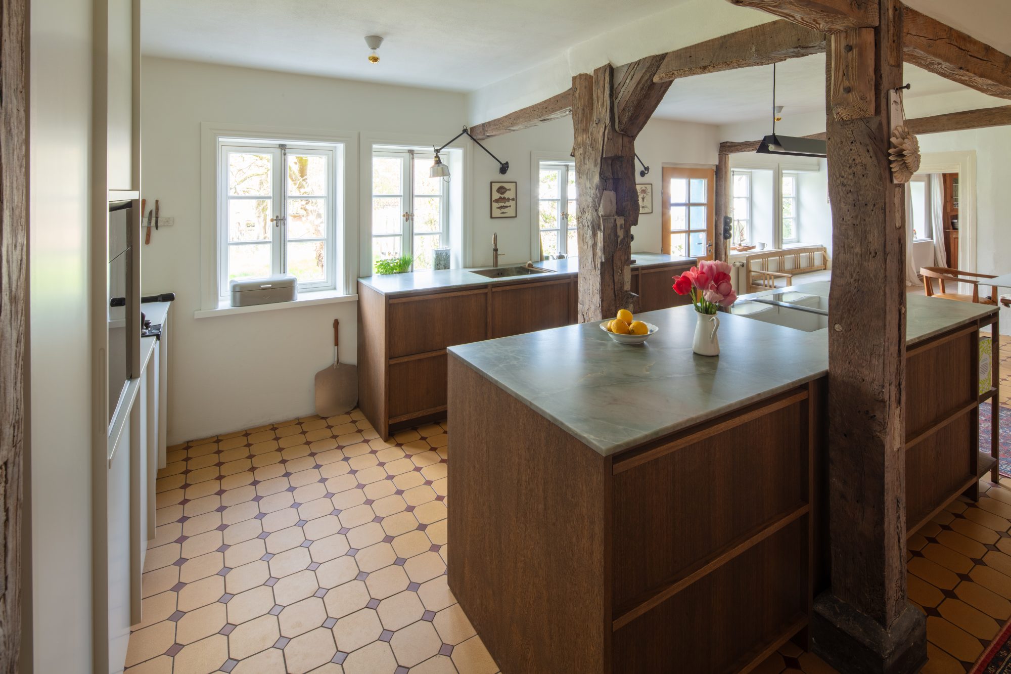 Blick auf die Kücheninsel mit Tulpen und Zitronenschale, umgeben von sichtbaren Holzbalken und einer Küchenzeile am Fenster.